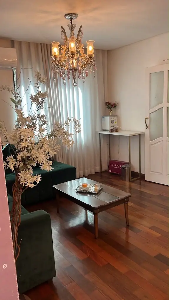 Sala de atendimento com sofá verde, mesa de centro de madeira e lustre de cristal
