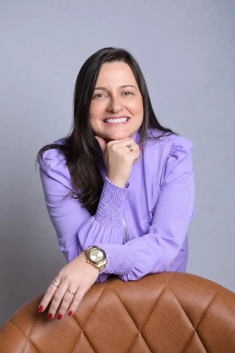 Viviane Nepomuceno sorrindo, de blusa lilás, com a mão apoiada no queixo
